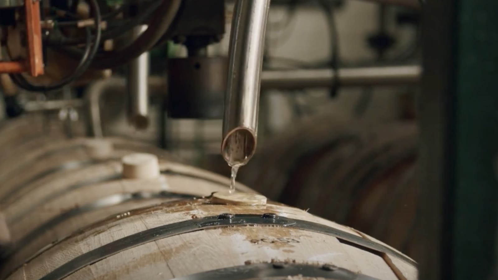 Spirit pouring from a steel pipe into a wooden barrel in a distillery