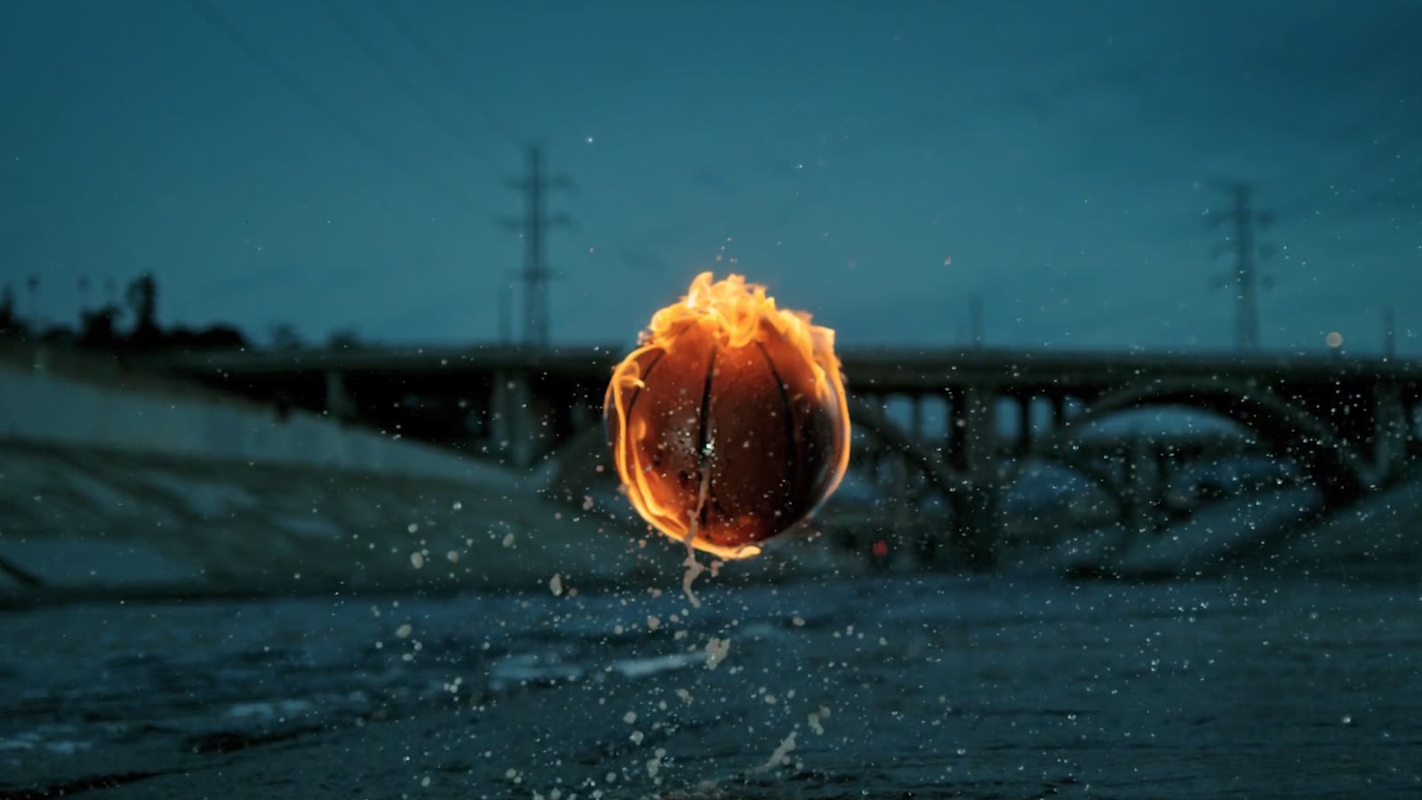 A basketball on fire mid-air over the LA River, bridge behind